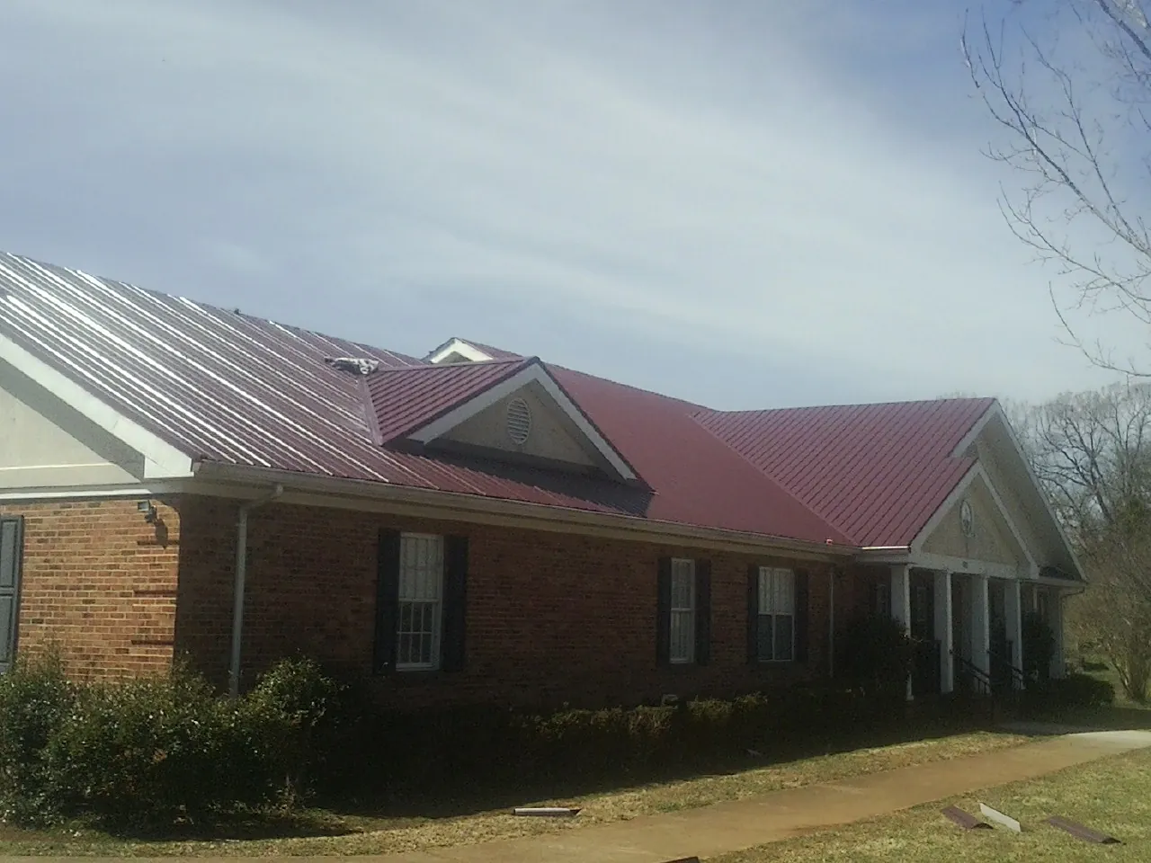 Red metal roof with gabled entries on a long brick building, from a Hail Damage Roof Repair job in Quincy