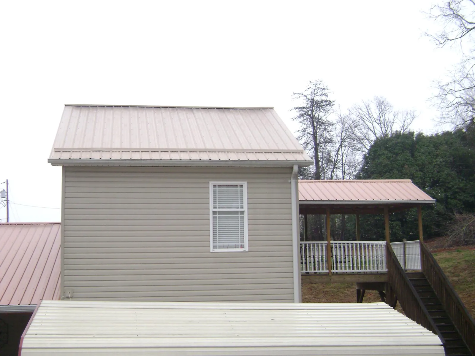 Tan metal roofs on a two story addition and attached porch, from a Roof Replacement job in Quincy